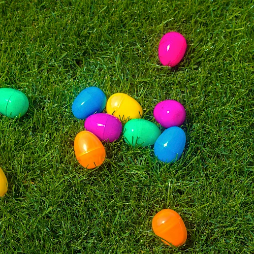 Colorful plastic Easter eggs are scattered on green grass, suggesting a festive or holiday-themed setting.