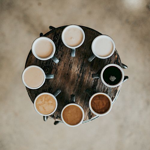 A round table with eight mugs of coffee, each varying in color and intensity, arranged in a circle.