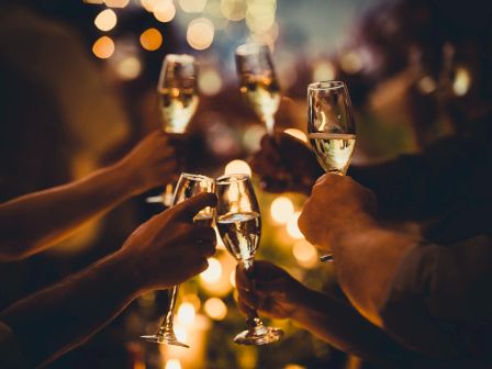 A group of people toasting with champagne flutes in a warm, festive celebration at night.