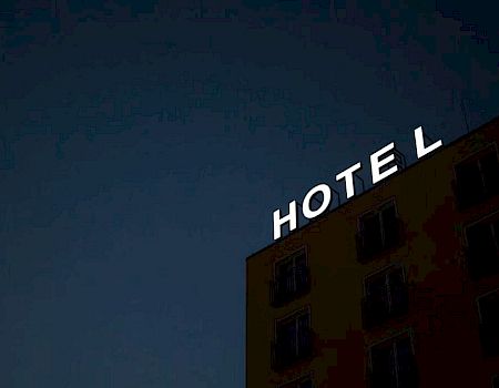 A building with a partially lit "HOTEL" sign at night, with the last letter "L" illuminated while the sign appears dark against the evening sky.