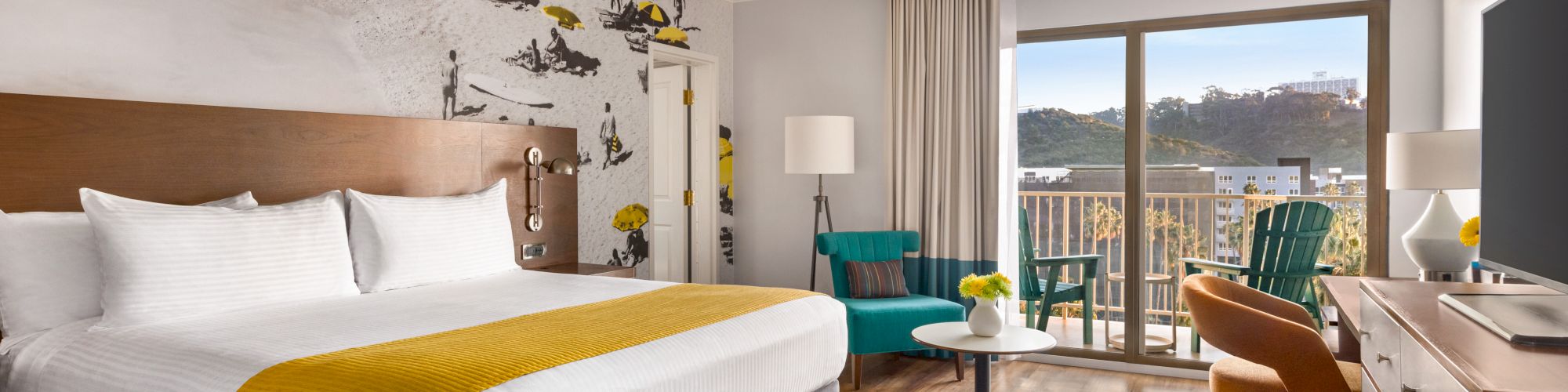 A modern hotel room with a large bed, stylish decor, a seating area, a balcony with a view, and a TV on a wooden dresser, creating a cozy atmosphere in a San Diego hotel.