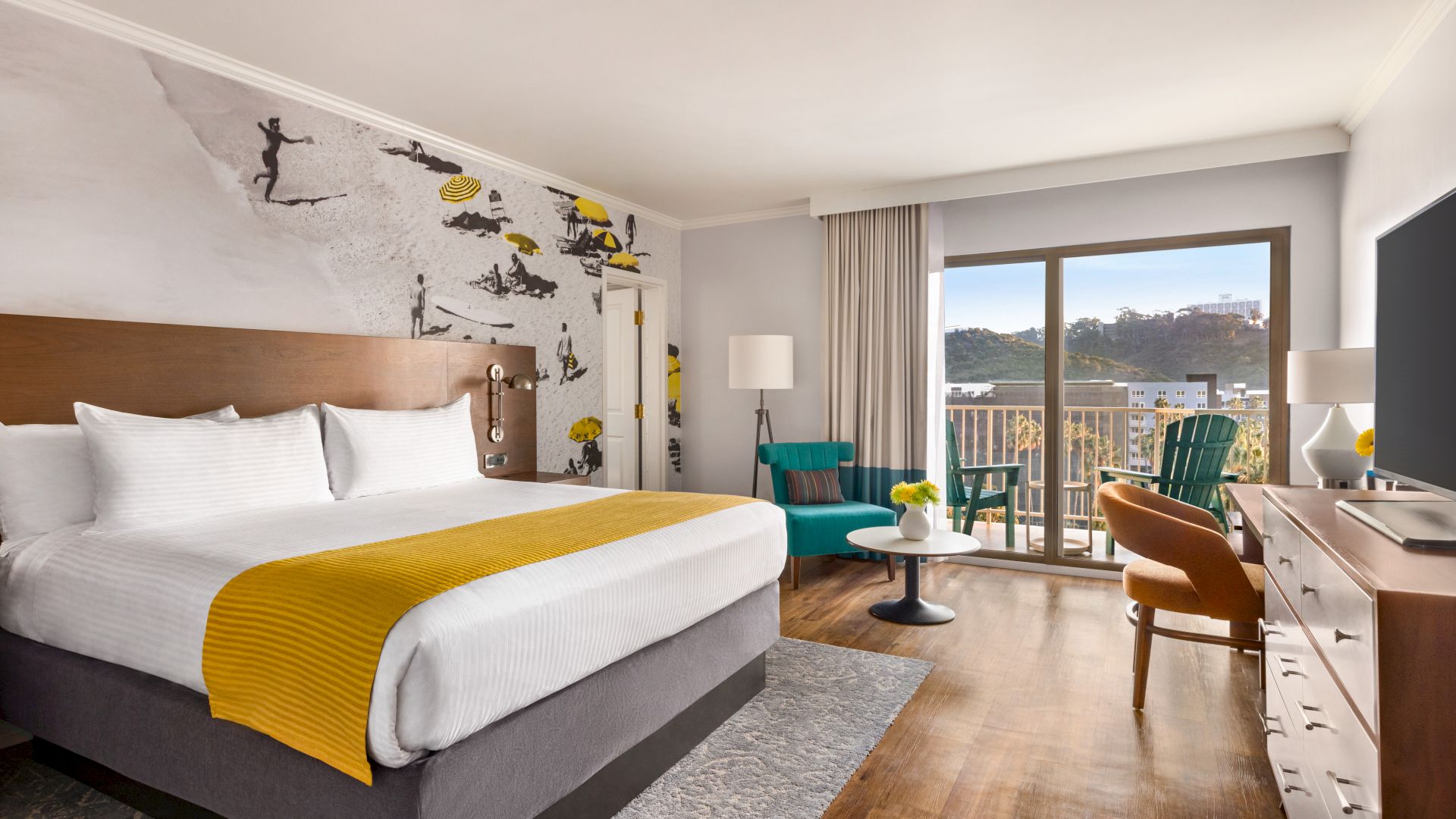 A modern hotel room with a large bed, vibrant accent decor, a seating area, and a balcony with a scenic view.
