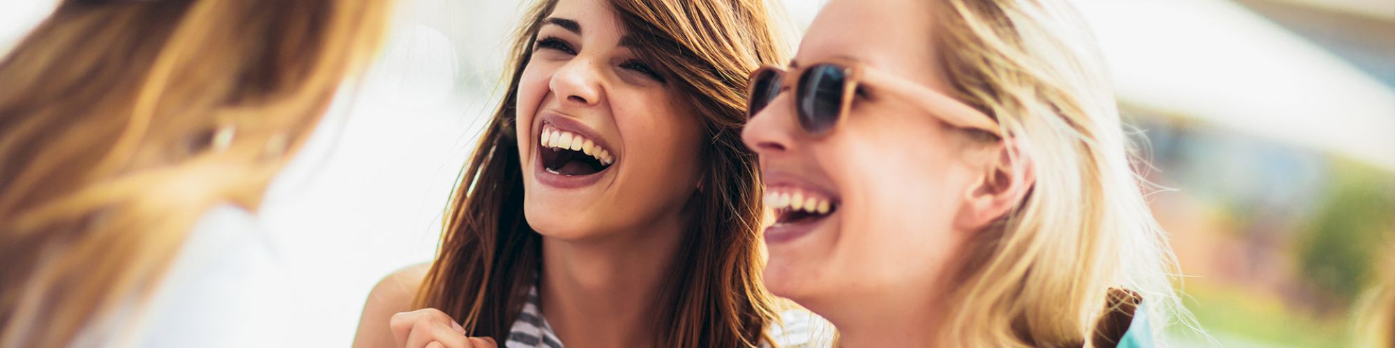 Three women are laughing and enjoying a good time together outdoors, each carrying shopping bags.