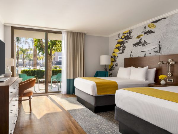 Modern hotel room with twin beds, sunny sliding doors to a pool view, and a graffiti mural on the wall.