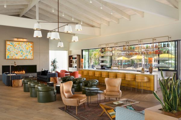A modern, cozy lounge with leather chairs, a bar area, a fireplace, and contemporary lighting. Various seating arrangements adorn the space.