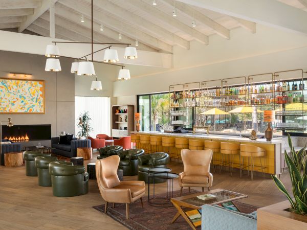 A modern, cozy lounge with leather chairs, a bar area, a fireplace, and contemporary lighting. Various seating arrangements adorn the space.