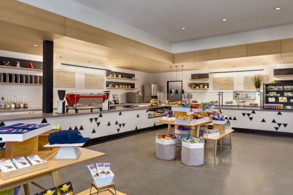The image showcases a modern café or shop interior with neatly arranged shelves, snacks, a coffee machine, and minimalist decor.