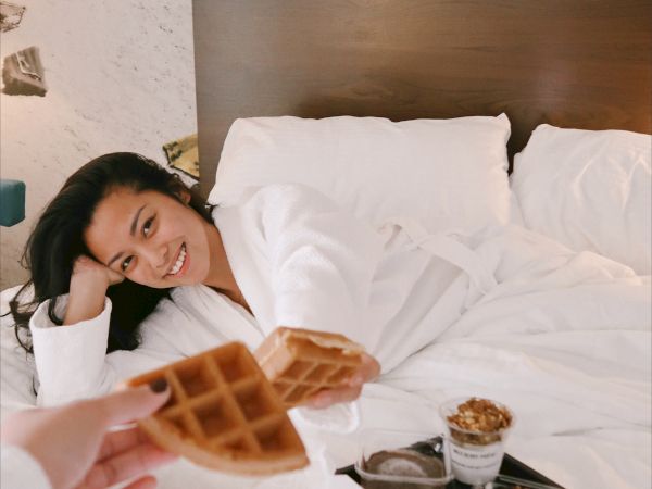 A person in bed is being offered waffles, with a breakfast tray nearby.