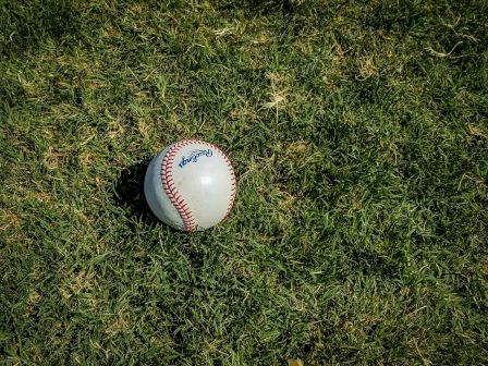 A white baseball with red stitching sits on green grass.