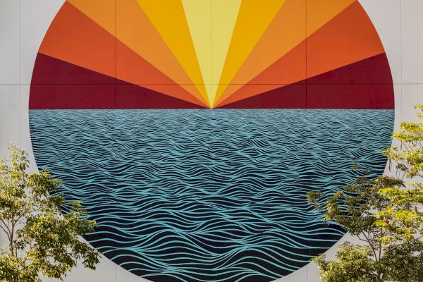 A mural depicting a large circle with waves and a radiant sun above. Green trees and plants are at the bottom of the image.