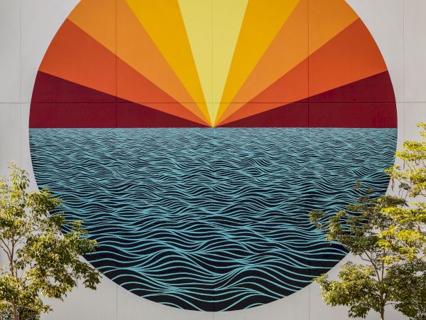 A mural depicting a large circle with waves and a radiant sun above. Green trees and plants are at the bottom of the image.