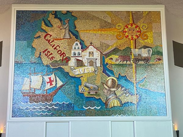 This image shows a colorful mural depicting historical scenes and landmarks of California, including a ship, a mission, a road, a miner, and a sun icon.