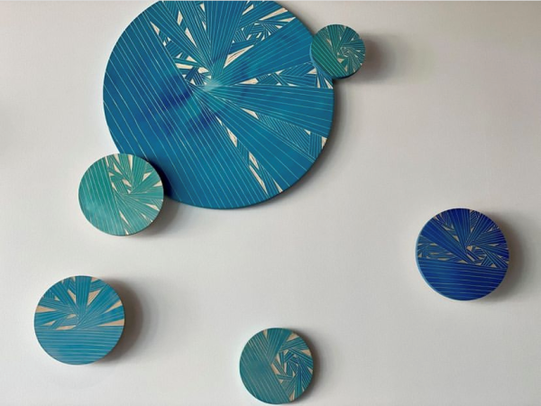 The image shows a wall with six circular art pieces in various shades of blue and teal, featuring intricate linear patterns and abstract designs.