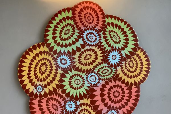 A vibrant, multi-colored geometric artwork is hanging on a wall under a light. The design features intricate spiral patterns in various colors.