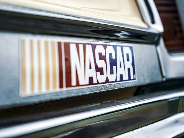 A vintage car with a NASCAR sticker on the bumper, chrome trim, and a classic grille reflecting light.