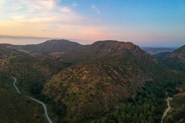 A scenic landscape featuring rolling hills, a winding dirt road, and a picturesque sky at sunset, with a serene, natural atmosphere.