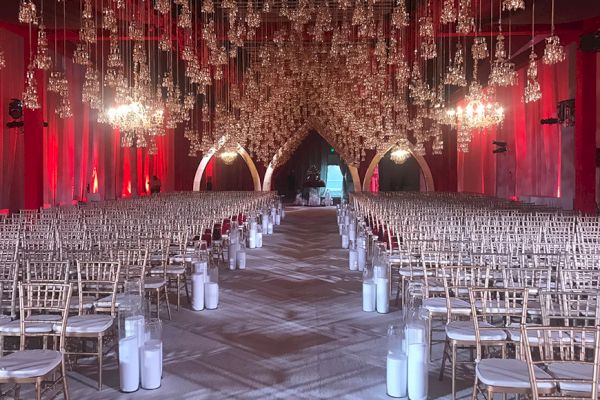 A grand indoor venue with arranged chairs, arches, chandeliers, and candles, highlighting an elegant setting for an event or ceremony.