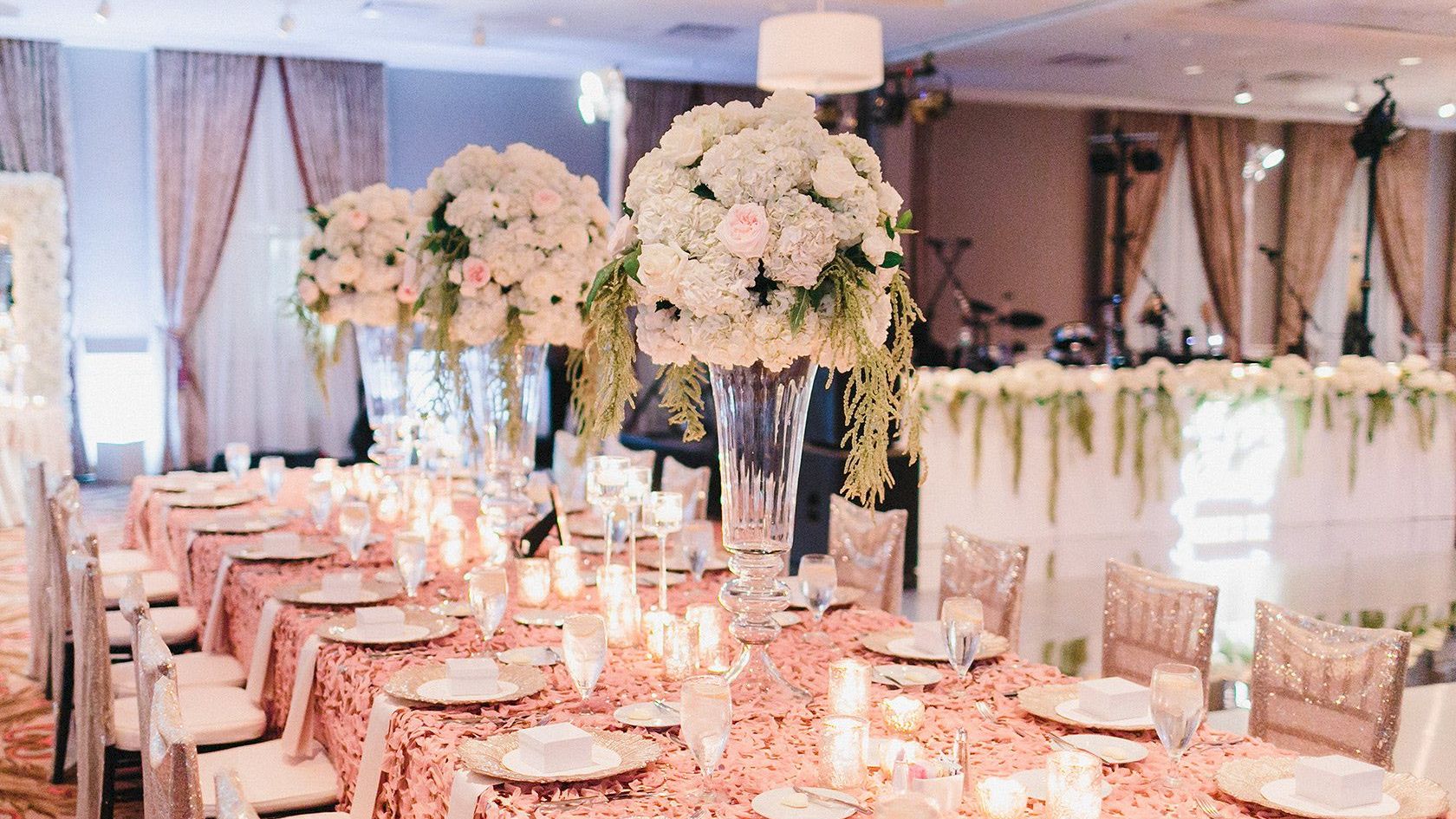 An elegantly set dining table with floral centerpieces, candles, and plates, surrounded by chairs in a well-decorated room ending the sentence.
