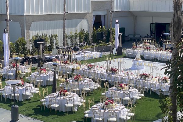 The image shows an outdoor event setup with decorated tables and chairs, floral centerpieces, and a dance floor ready for guests.