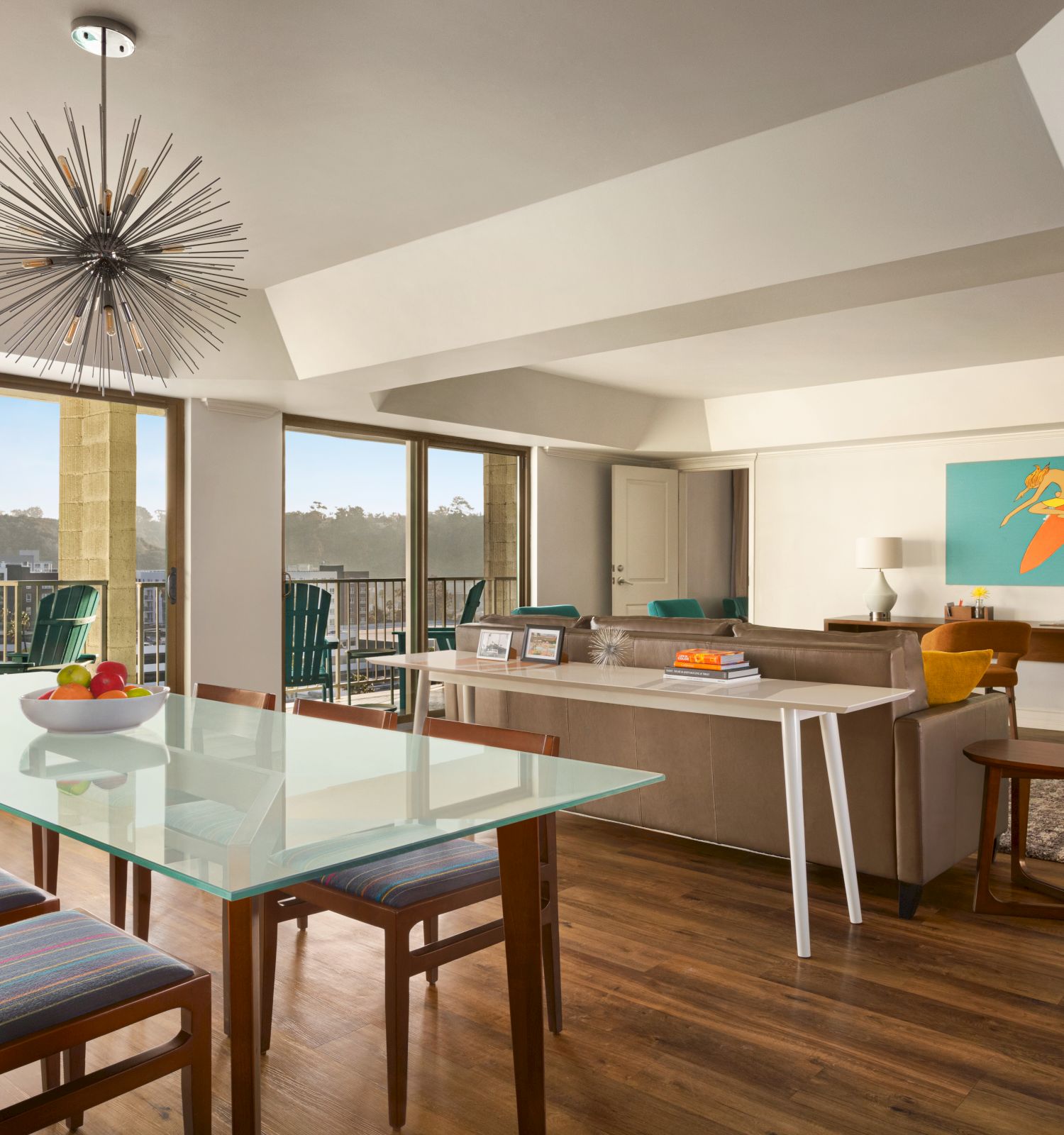 A modern living and dining area with large windows, contemporary furniture, a glass dining table with chairs, and a vibrant wall painting in the Best Resort in San Diego.
