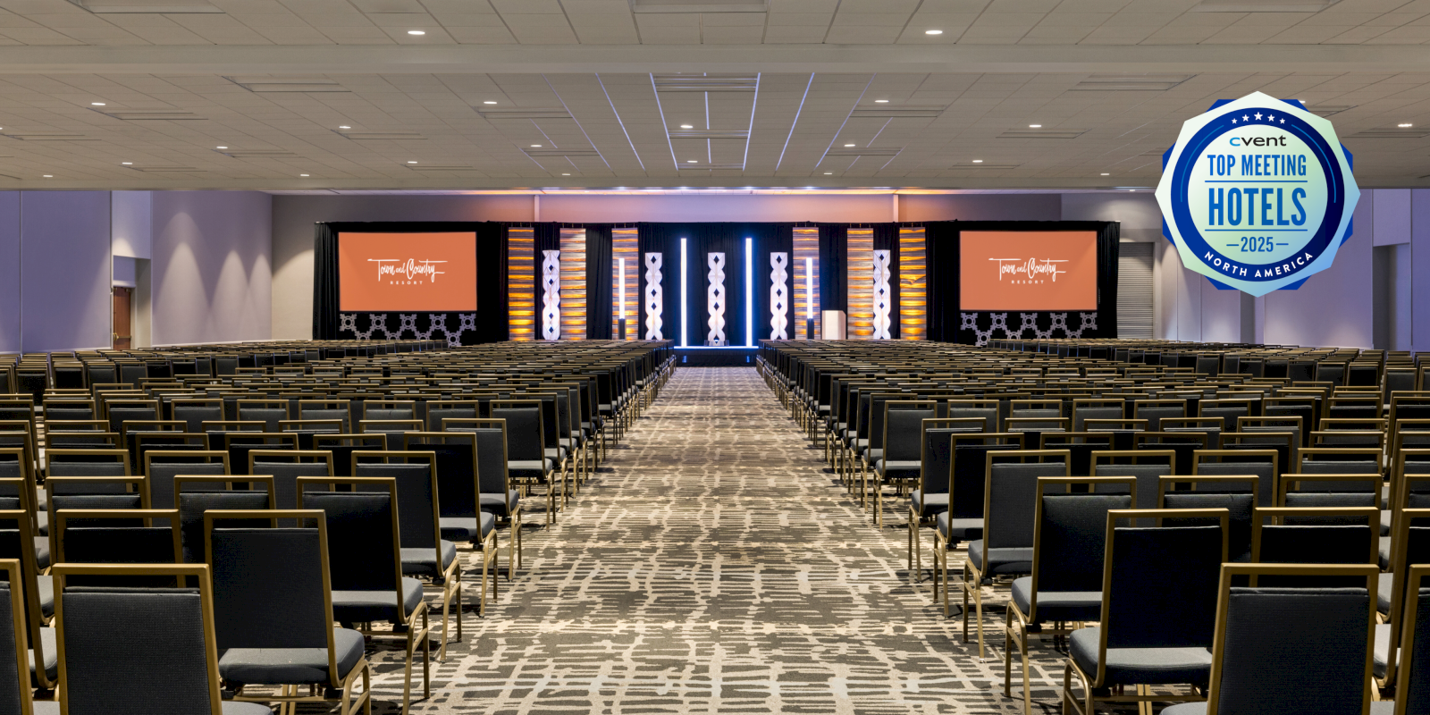 An empty conference room with rows of chairs facing a stage and a "Top Meeting Hotels 2015" badge displayed on the right side.