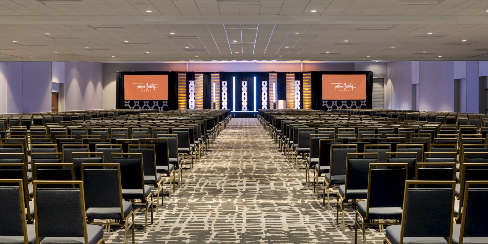 A large conference room with rows of chairs facing a stage with two screens displaying text and graphics, set up for a presentation or event. Award winning meeting and event space in San Diego for groups from 30 to 3,000.