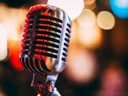 A classic vintage microphone on a stand, ready for a live performance, with colorful blurred lights in the background.