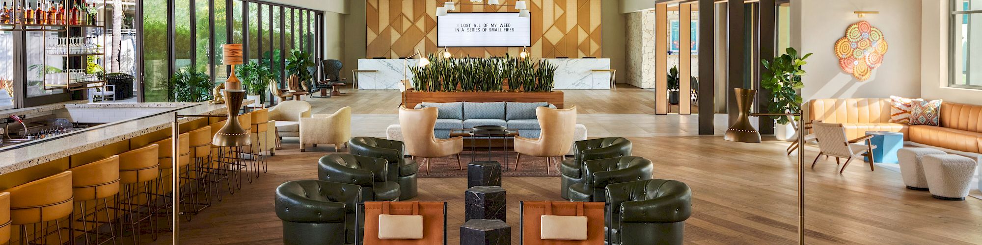 The image shows a stylish, spacious lounge with modern seating, a bar area, large windows, and contemporary decor, featuring a mix of cozy furniture.