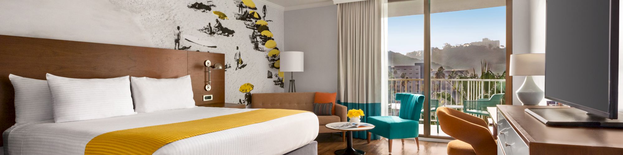 A modern hotel room featuring a large bed, colorful decor, a wall mural of skiers, a sitting area, a balcony, and a flat-screen TV.