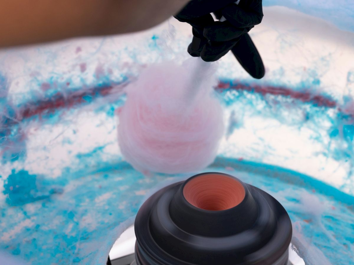 Someone is handling a pink-tinted object over a blue-tinted surface, with a dark container nearby inside a circular setup, ready to dispense.