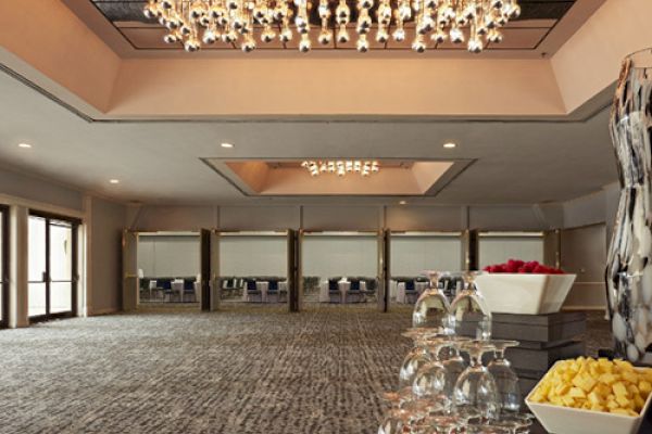 The image depicts an elegant, empty banquet room with a large chandelier, tables set with fruits and drinkware, and wall art.