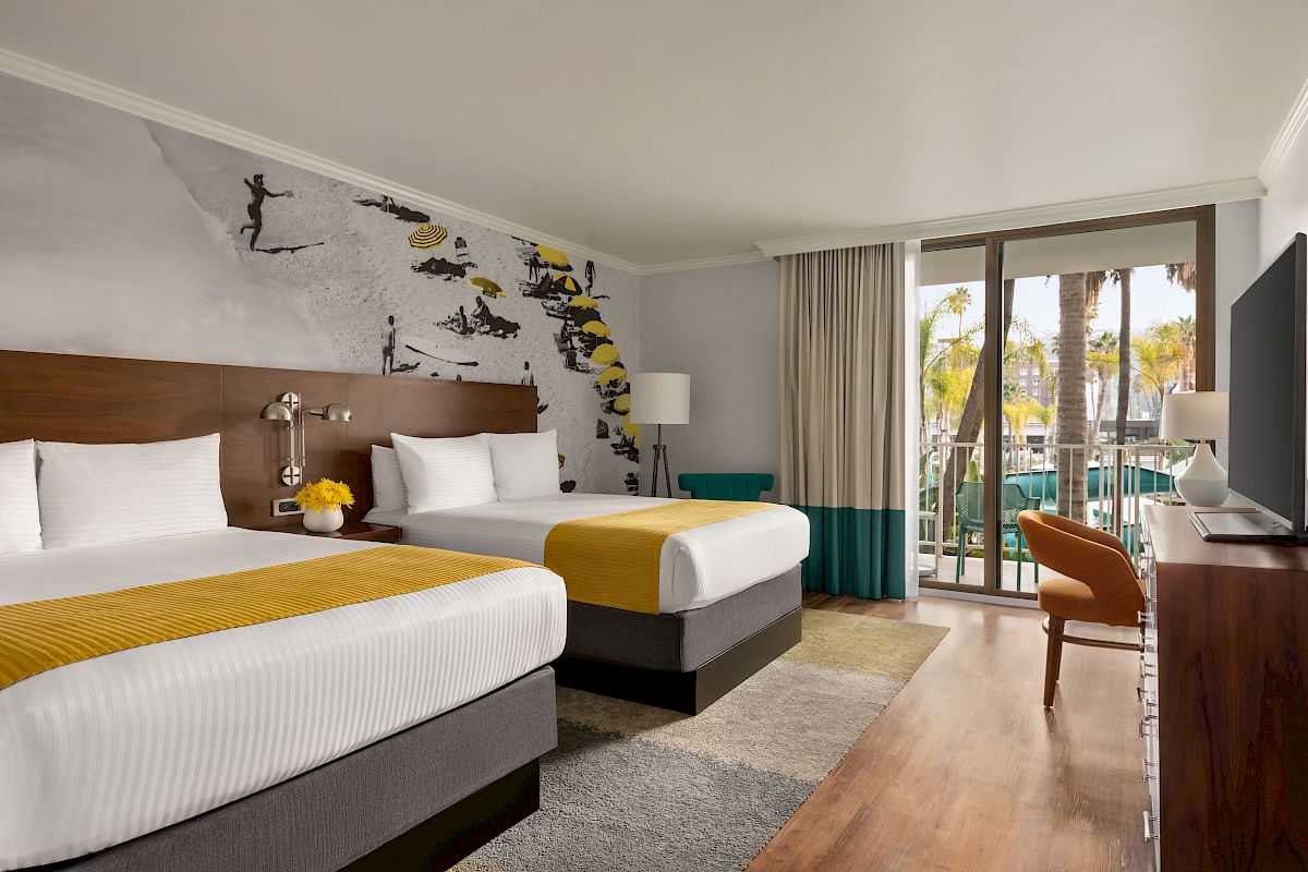 A modern hotel room with two beds, a yellow-striped mural wall, and balcony doors showing palm trees outside.