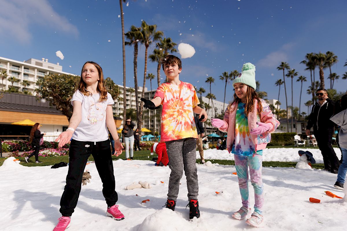 Kids joyfully playing in the snow outdoors with snow flying and palm trees in the background on a sunny day!