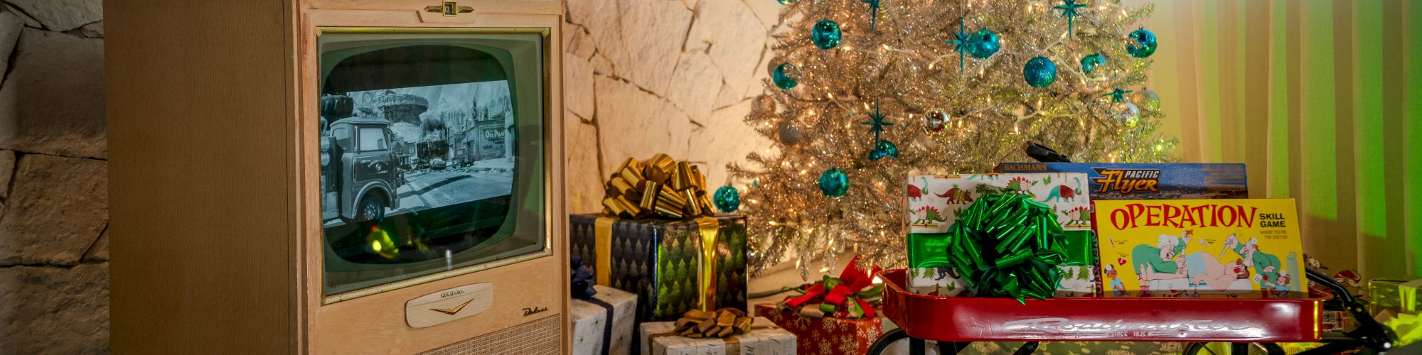 Vintage room with a Christmas tree, presents, a wagon, and an old TV displaying a black-and-white image.