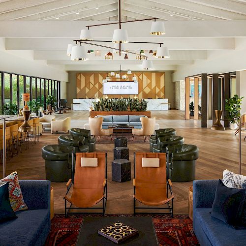 This image shows a spacious, modern lounge area with various seating options, a bar on the left, and a large window providing natural light.