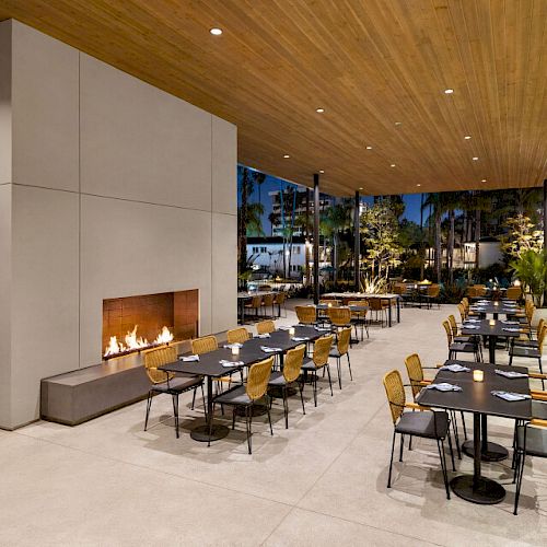 An outdoor dining area with a fireplace, wooden ceiling, and several tables and chairs set for dining during the evening.
