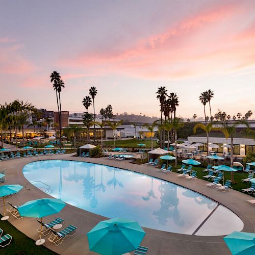 This image shows a serene pool area surrounded by lounge chairs and turquoise umbrellas, with palm trees and a sunset sky in the background.