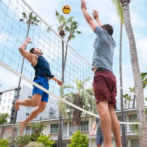 Two people are playing beach volleyball. One is jumping to spike the ball while the other is attempting to block at the net.