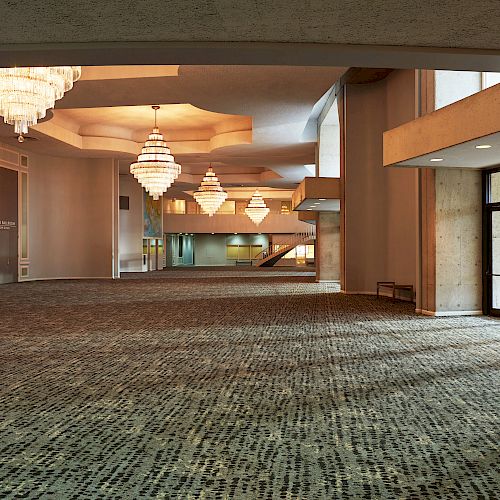 An elegant, spacious lobby or event hall with large chandeliers, modern carpet, a mural on the wall, and glass doors leading outside.