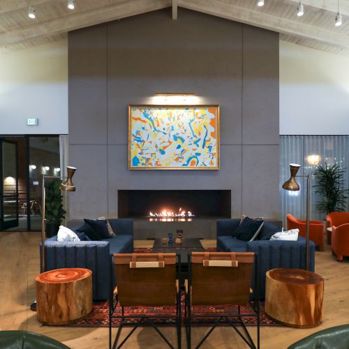 A stylish living room features modern furniture, a central fireplace, abstract artwork, and cozy seating arrangements, creating a welcoming atmosphere.