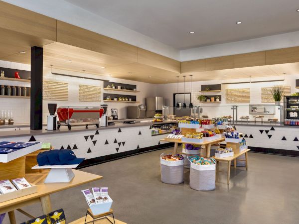 A modern café or store with shelves of snacks, a coffee machine, and minimalist decor. There are tables displaying various products.