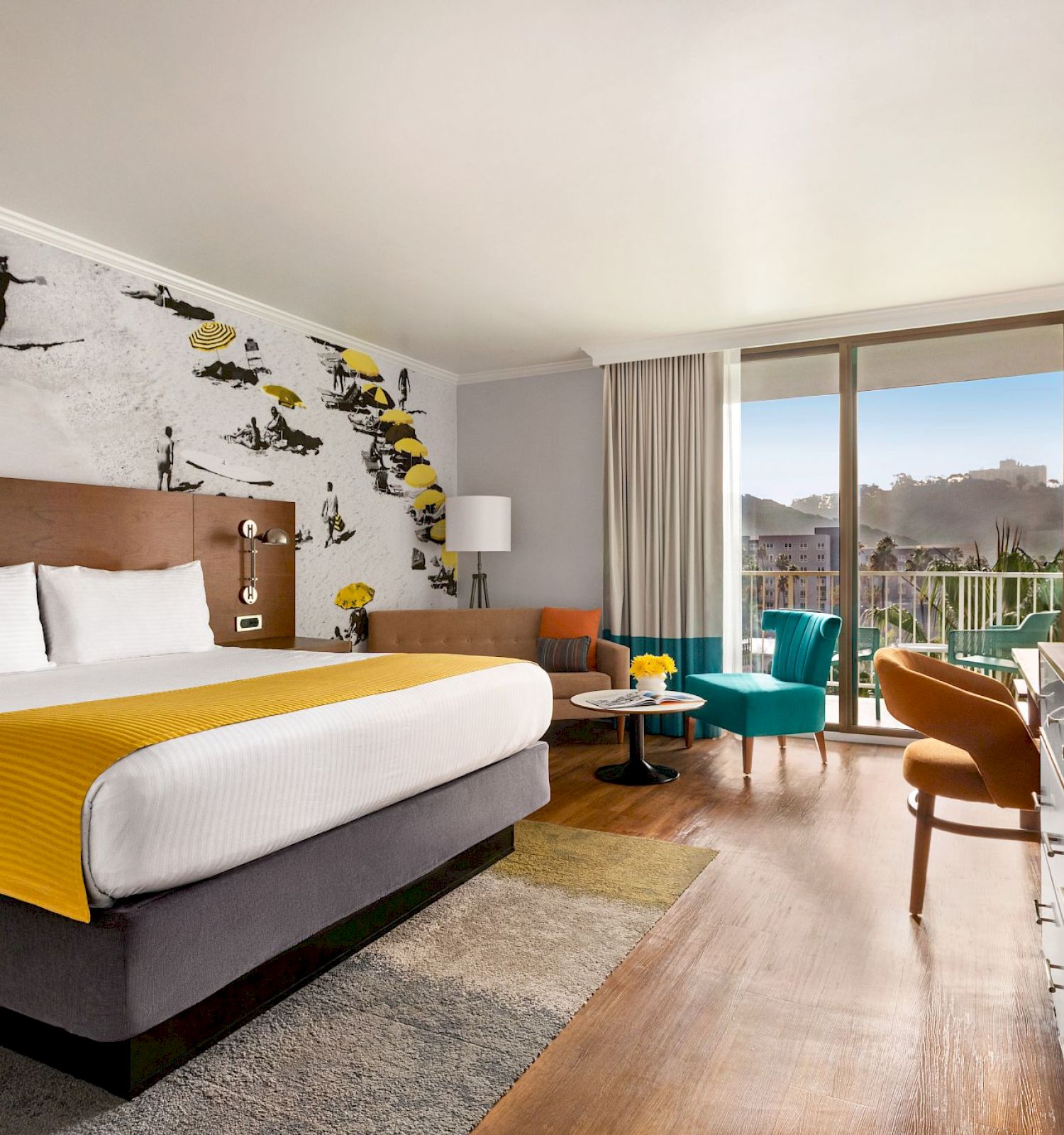A modern hotel room with a large bed, a ski-themed mural, a flat-screen TV, a seating area, and a balcony with a scenic view.