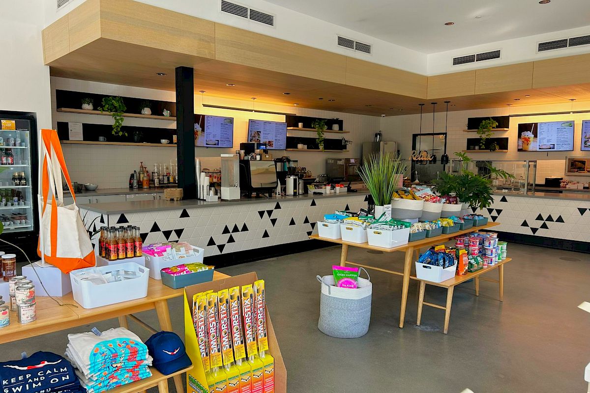 A modern caf&eacute; counter with espresso machines, shelves of drinks, and lots of snacks and plants on display.