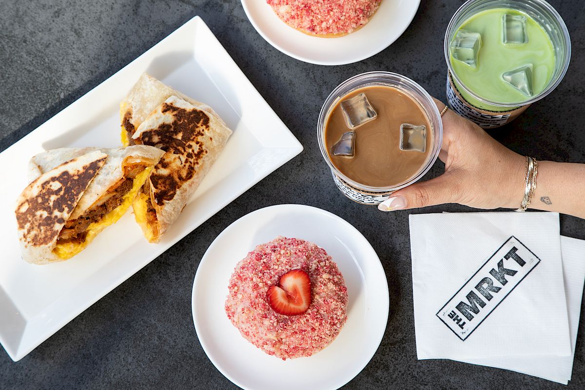 A breakfast spread with quesadilla, a strawberry donut, green matcha and iced coffee drinks on a table.