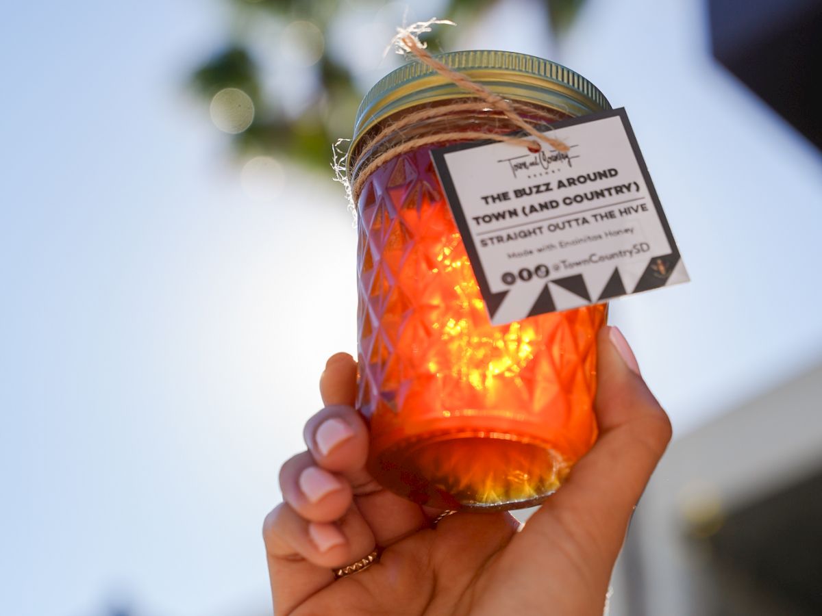 A hand holds an orange honeycomb-style container/tin with a label reading &ldquo;The Buzz Around Town (and Country).&rdquo;