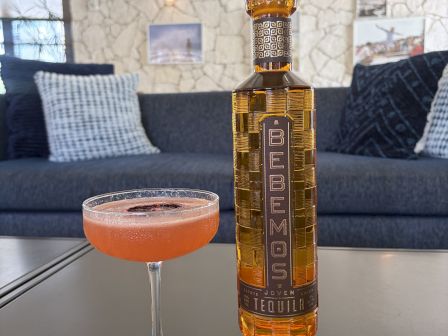 A tequila bottle and an orange cocktail in a glass on a bar table in a cozy lounge setting.