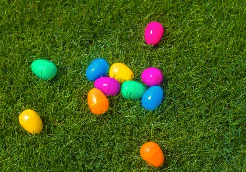 Colorful plastic Easter eggs are scattered on green grass, suggesting a festive or holiday-themed setting.