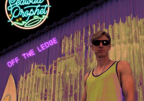 The image depicts a person in sunglasses and a tank top standing beside a wall with graffiti. The text reads "Seawall Prophet" and "Off The Ledge."