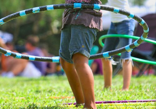 Children are playing with hula hoops on a grassy field, engaging in outdoor fun and enjoying the sunny day.
