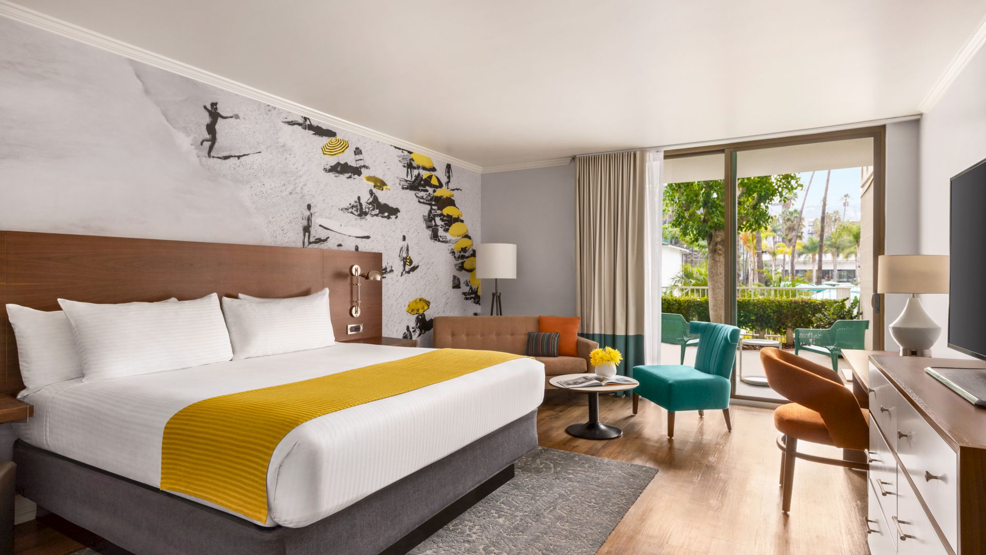 A modern hotel room with a large bed, stylish wall art, comfortable seating area, and a window overlooking a green outdoor space ends the sentence.